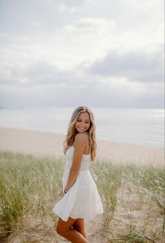 a woman standing on top of a sandy beach next to the ocean wearing a white dress