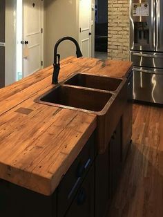 a kitchen with an island made out of wood and stainless steel appliances in the background