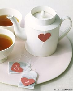 two cups of tea on a plate with hearts and stickers attached to the mugs