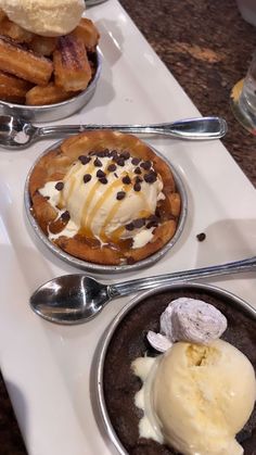 three different desserts are sitting on a white plate with silver spoons and two bowls filled with ice cream