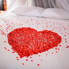 a heart shaped bed with red petals on the top and white sheets in the background