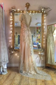 two dresses are on display in front of a mirror with lights strung from the ceiling