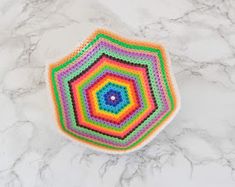 a multicolored crocheted dishcloth sits on a marble countertop, with a circular hole in the center