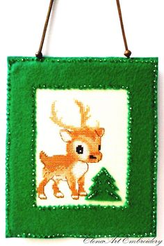 a cross stitch picture hanging on a wall with a deer in the center and a green frame around it