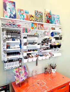 an orange table in front of a wall with art supplies on it and shelves above