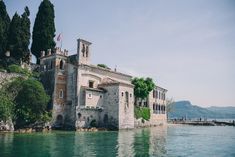 an old building sitting on top of a lake next to a forest filled mountain side