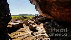 an open window in the side of a rock formation with grass and sky in the background