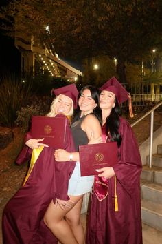 three women in graduation gowns holding diplomas and posing for the camera at night