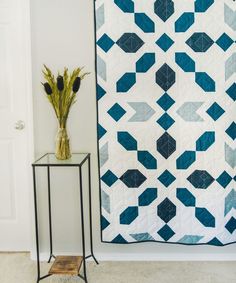 a blue and white quilt sitting on top of a table next to a vase with flowers