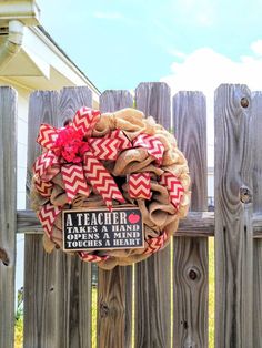 a red and white wreath with teacher's name hanging on a wooden picket fence