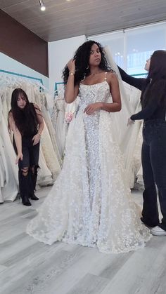 a woman in a white wedding dress standing next to a man and another person looking at dresses