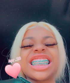 a woman with blonde hair and blue braces holding a pink heart in front of her mouth