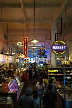 people are walking through an indoor market with neon signs