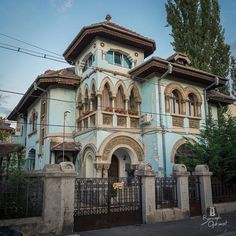 an old blue and white building with iron fence around it's perimeter in front of a tree