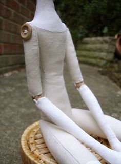 a white doll sitting on top of a wicker basket