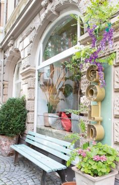 a wooden bench sitting in front of a window filled with potted plants and flowers