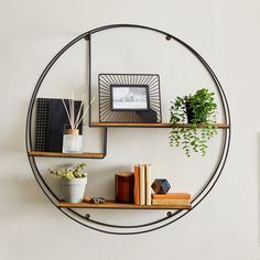 a circular metal shelf with books and plants on it next to a wall mounted clock