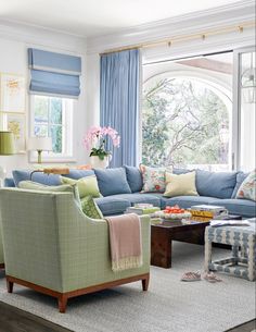 a living room filled with lots of furniture next to a large window covered in blue curtains