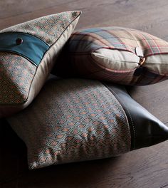 three pillows stacked on top of each other in different colors and patterns, sitting on a wooden floor