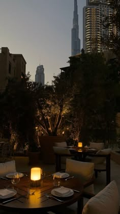 an outdoor dining area with tables and chairs in front of the city skyline at night