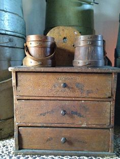 an old wooden dresser with two buckets on top of it and another metal container sitting next to it