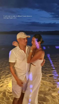 a man and woman standing on the beach at night with their arms around each other