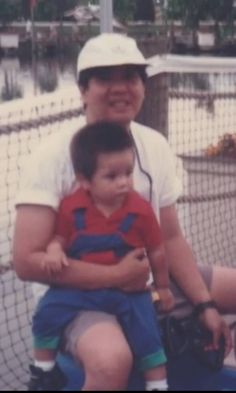 a man holding a small child on top of a tennis court with net in the background