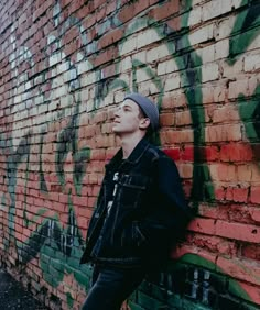 a young man leaning against a brick wall with graffiti on it and looking up to the sky