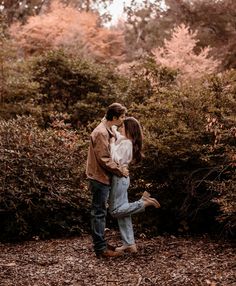 an engaged couple kissing in the woods during their engagement photo session at sunset with golden leaves on the ground