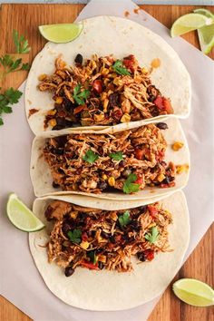 three shredded pork tacos on a white plate with limes and cilantro