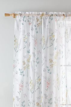 a white curtain with flowers on it hanging in front of a window, next to a wooden rod