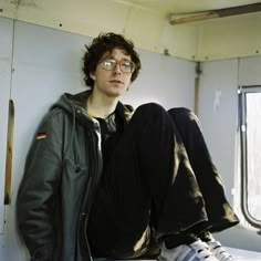 a young man sitting on top of a bed in a room with white walls and windows