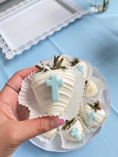 a hand holding a white chocolate covered in frosting with a cross on the top