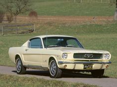 an old ford mustang sitting on the side of a road in front of a grassy field