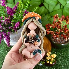 a hand holding a small figurine in front of some plants