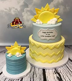 two tiered birthday cake with sun and cloud decoration on top, sitting next to each other