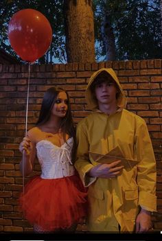 two people in costumes standing next to each other near a brick wall with a red balloon