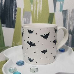 a white cup with bats on it sitting on a plate next to some blue and green candies