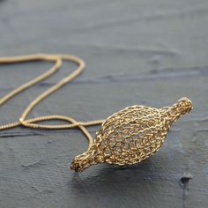 a gold necklace with a small bird on it's back end, sitting on a wooden surface