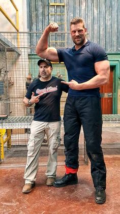 two men standing next to each other in front of a caged area with one man flexing his muscles