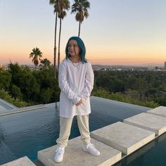 a woman with blue hair standing on concrete steps next to a pool and palm trees