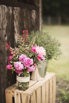 two vases with flowers are sitting on a wooden crate