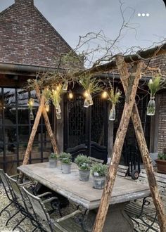 an outdoor dining area with potted plants on the table and lights hanging from the roof