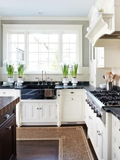 a white kitchen with black counter tops and wooden floors in front of two large windows