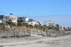 a row of houses on the beach with fenced in area and sand behind them