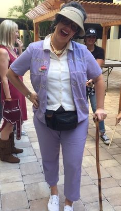 a woman in purple pants and white shirt holding a cane while standing on a brick walkway