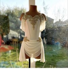 a white dress with gold beading on the shoulders and shoulder, sitting in front of a window