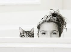 a girl with her cat peeking out from behind the bathtub