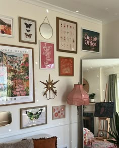 a living room filled with lots of framed pictures on the wall above a couch and lamp