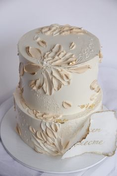 a three tiered cake with white frosting and gold leaves on the bottom layer